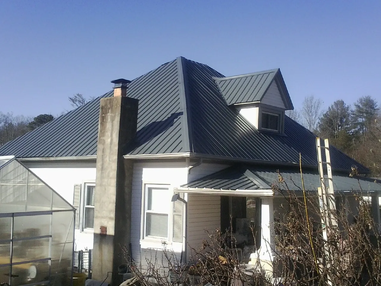Dark blue standing seam metal roof on a white farmhouse with dormer — Slate & Tile Roof Repair by Roofing Brothers in Guyton