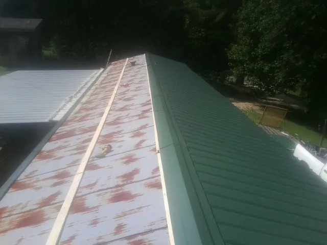 Old rusted panels beside newly installed green metal roofing — Wind Damage Roof Repair by Roofing Brothers in Guyton
