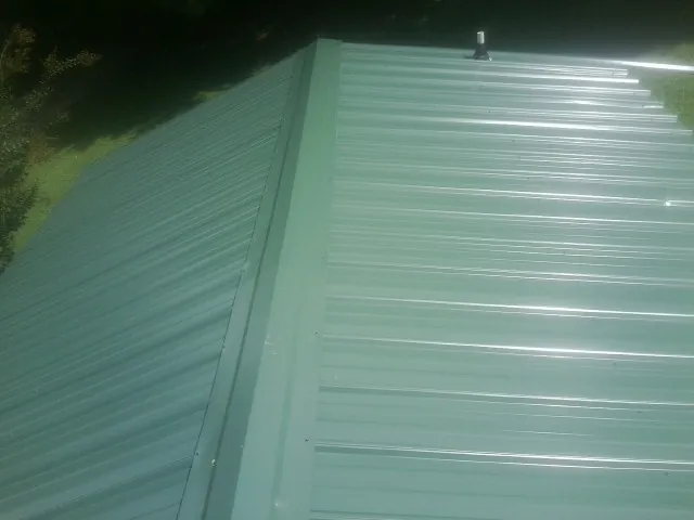 New green metal panels meeting at the ridge of a roof — Flat Roof Repair work by our crew in Guyton
