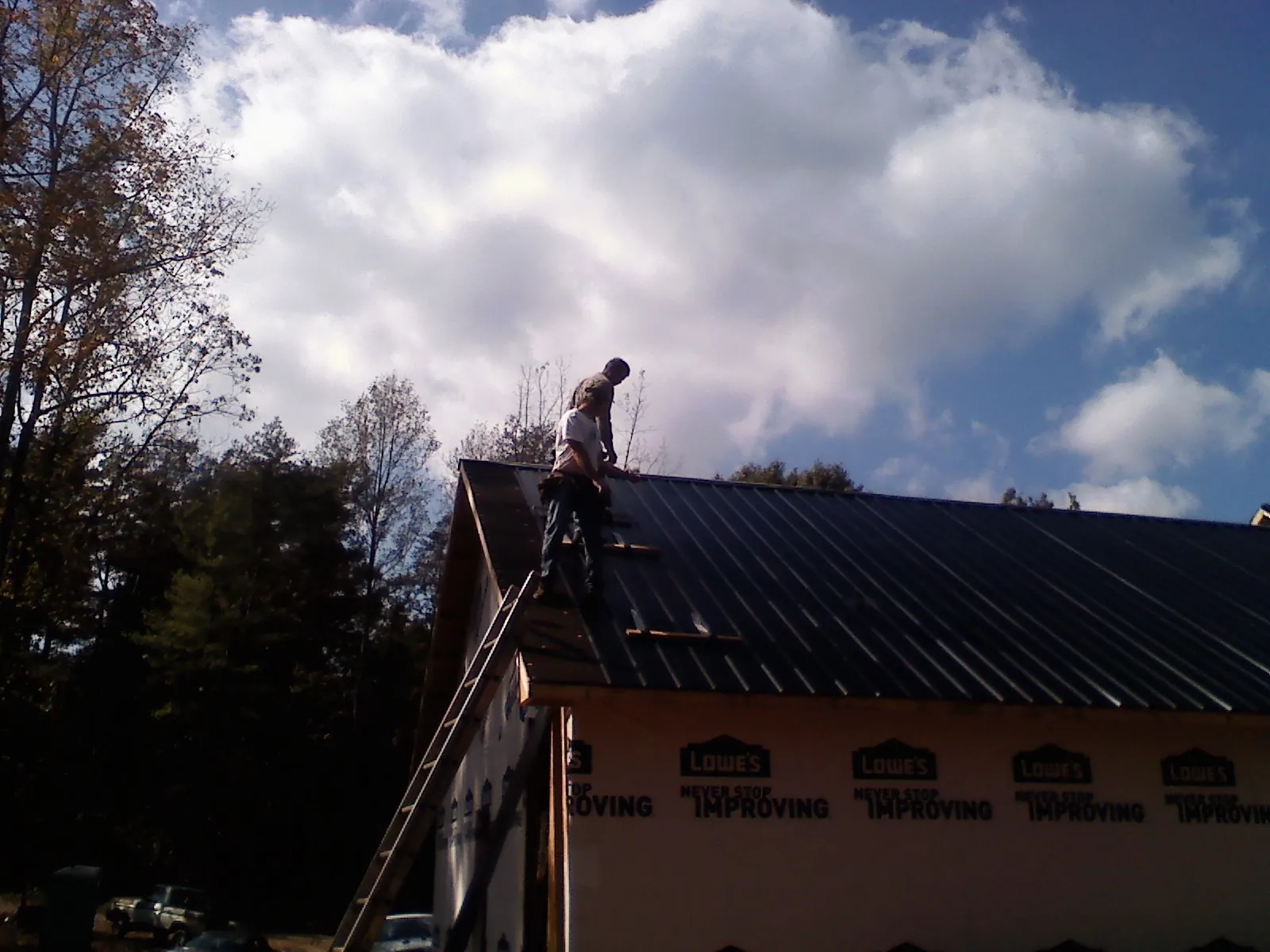 Roofer fastening dark metal panels high against a cloudy sky, from a Roof Inspection job in Guyton