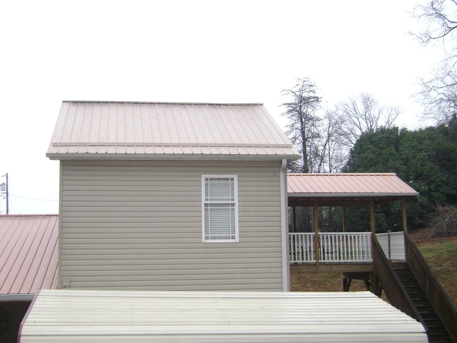 Tan metal roofs on a two story addition and attached porch, from a Roof Replacement job in Guyton